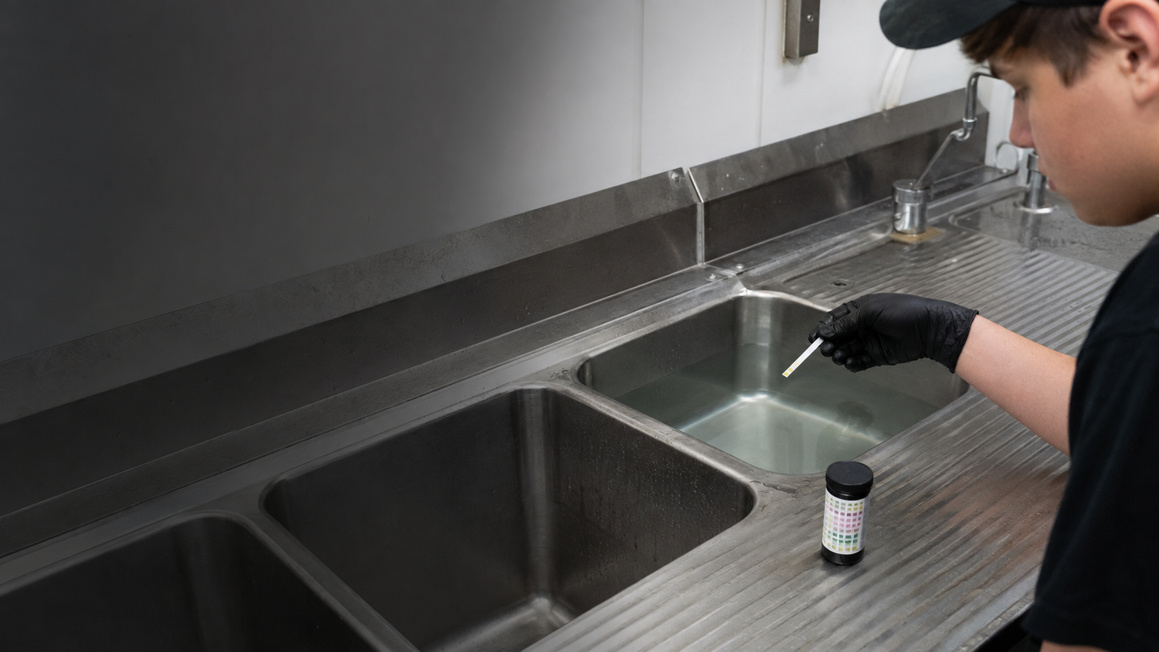 Teenage Krave employee verifying sanitizer with the correct test strip at the three-compartment sink